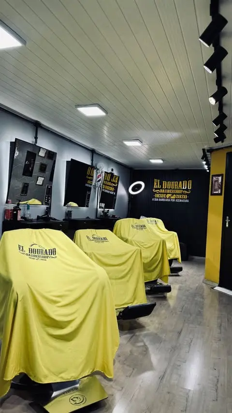 Interior da El Dourado Barbershop com cadeiras cobertas e letreiro dourado